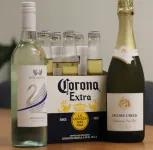 A Bottle Of Corona Extra Alongside Two Bottles Of Red Wine On A Wooden Surface